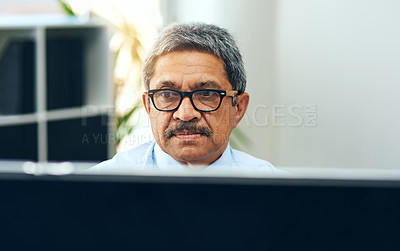 Buy stock photo Shot of a focussed mature man working on a computer while being seated at a desk inside of a building during the day