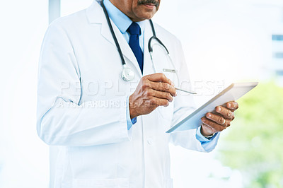 Buy stock photo Shot of an unrecognizable male doctor browsing on a digital tablet inside of a hospital during the day