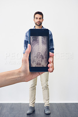 Buy stock photo Shot of an unrecognizable person holding a phone displaying an x-ray of a carefree young man standing against a grey background