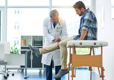 Buy stock photo Shot of a confident mature male doctor running tests on a patient inside of a examination room during the day