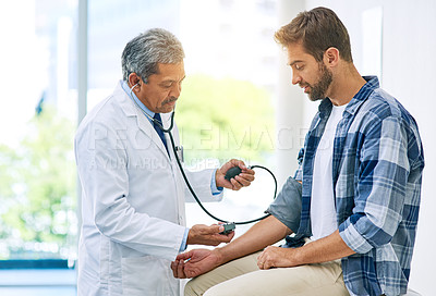Buy stock photo Shot of a confident mature male doctor running tests on a patient inside of a examination room during the day