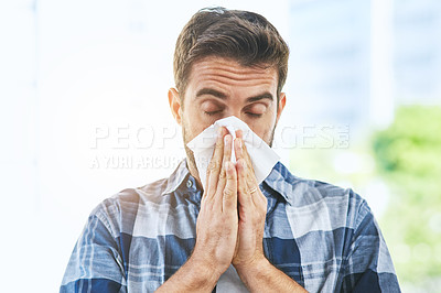 Buy stock photo Portrait of an uncomfortable looking young man blowing his nose with a tissue inside of a building during the day