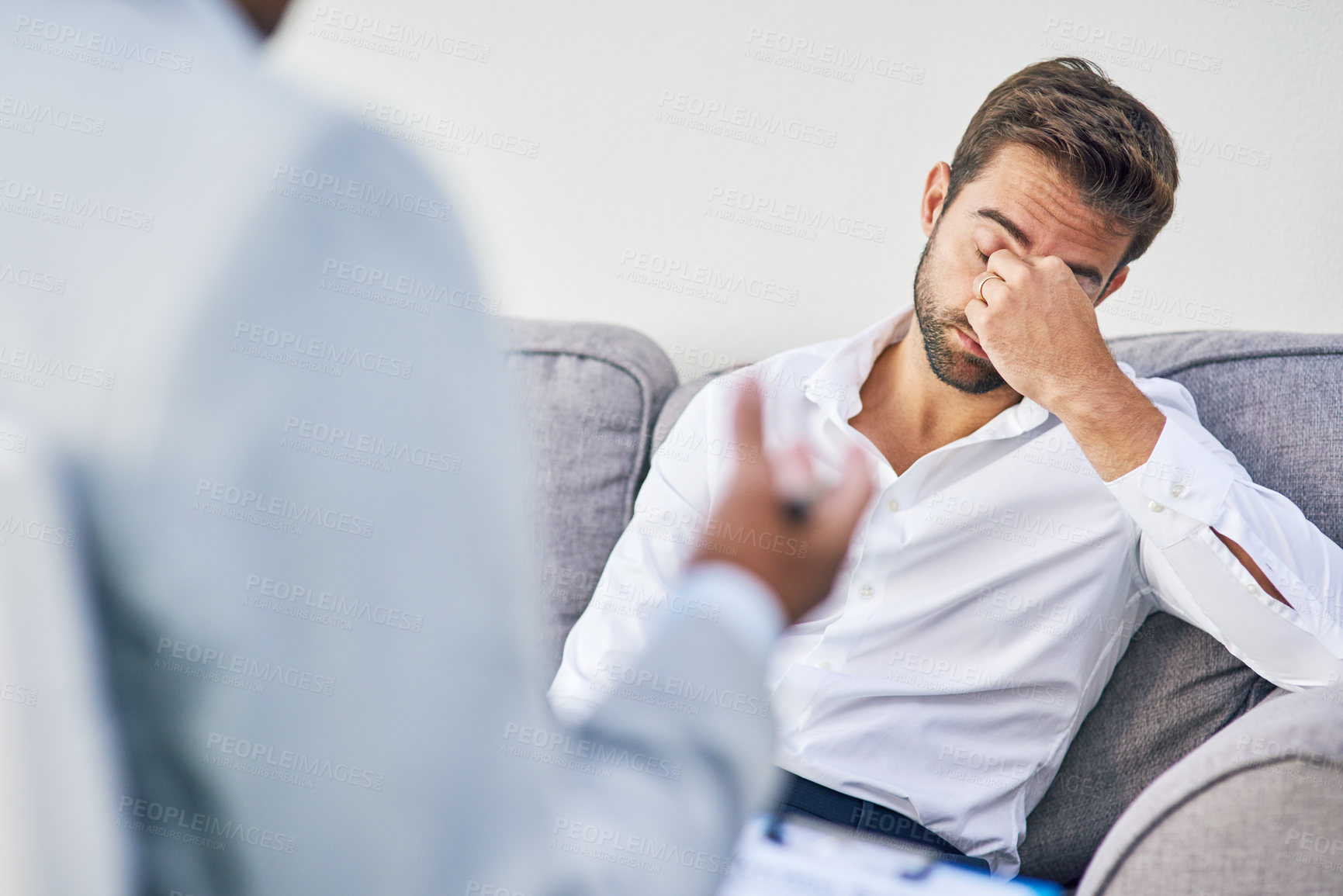 Buy stock photo Shot of an stressed out young man having a discussion with his doctor while being seated on a sofa inside of a doctor's office during the day