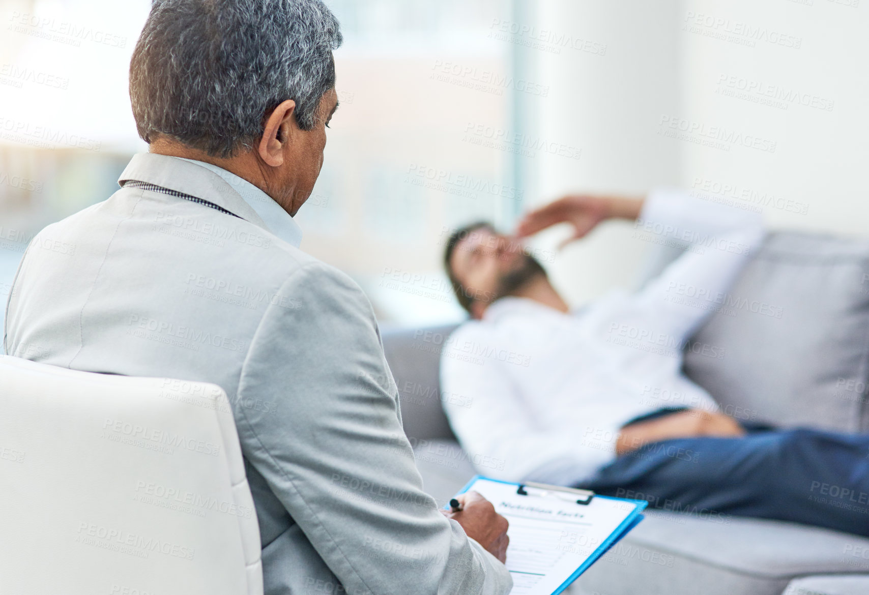 Buy stock photo Shot of an stressed out young man having a discussion with his doctor while lying on a sofa inside of a doctor's office during the day