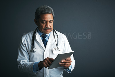 Buy stock photo Studio shot of a mature doctor using a digital tablet against a gray background