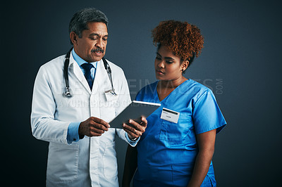 Buy stock photo Studio shot of two doctors using a digital tablet together against a gray background