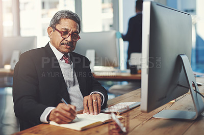 Buy stock photo Shot of a mature businessman writing notes while working on a computer in an office