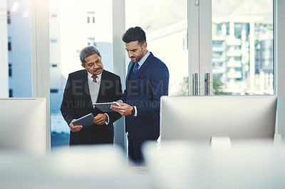 Buy stock photo Shot of two businessmen working on a digital tablet in an office