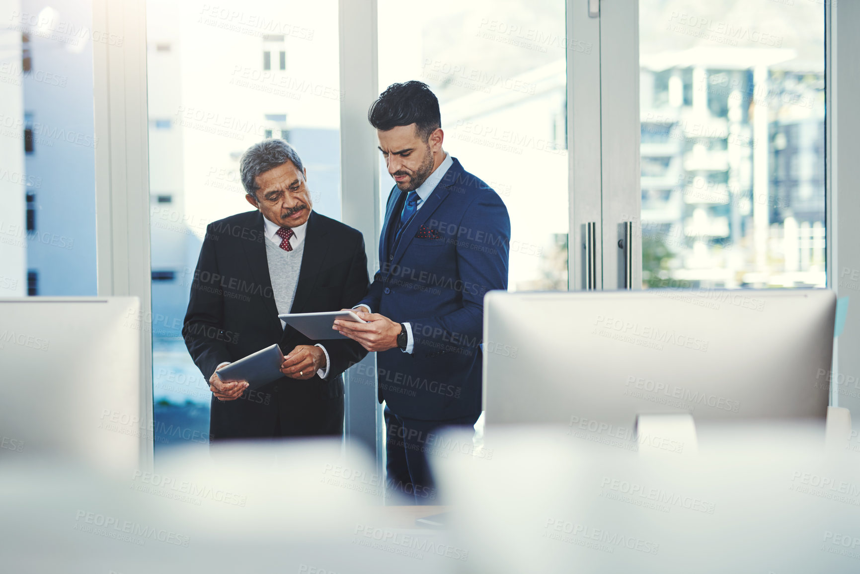 Buy stock photo Shot of two businessmen working on a digital tablet in an office