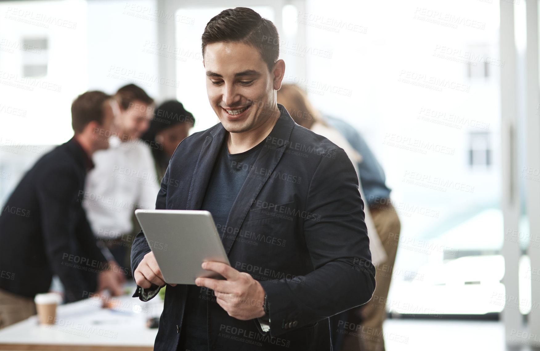 Buy stock photo Shot of a young businessman using a digital tablet in an office with his colleagues in the background