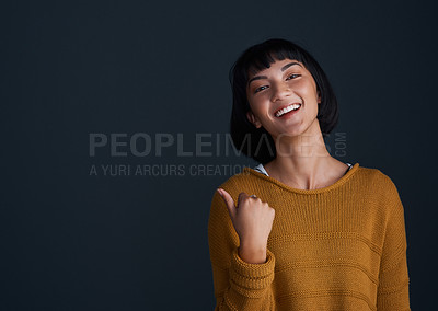 Buy stock photo Studio shot of an attractive young woman pointing against a dark background