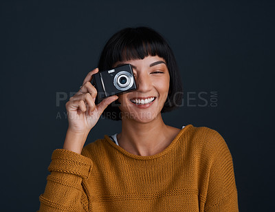 Buy stock photo Studio portrait of a young woman using a camera against a dark background