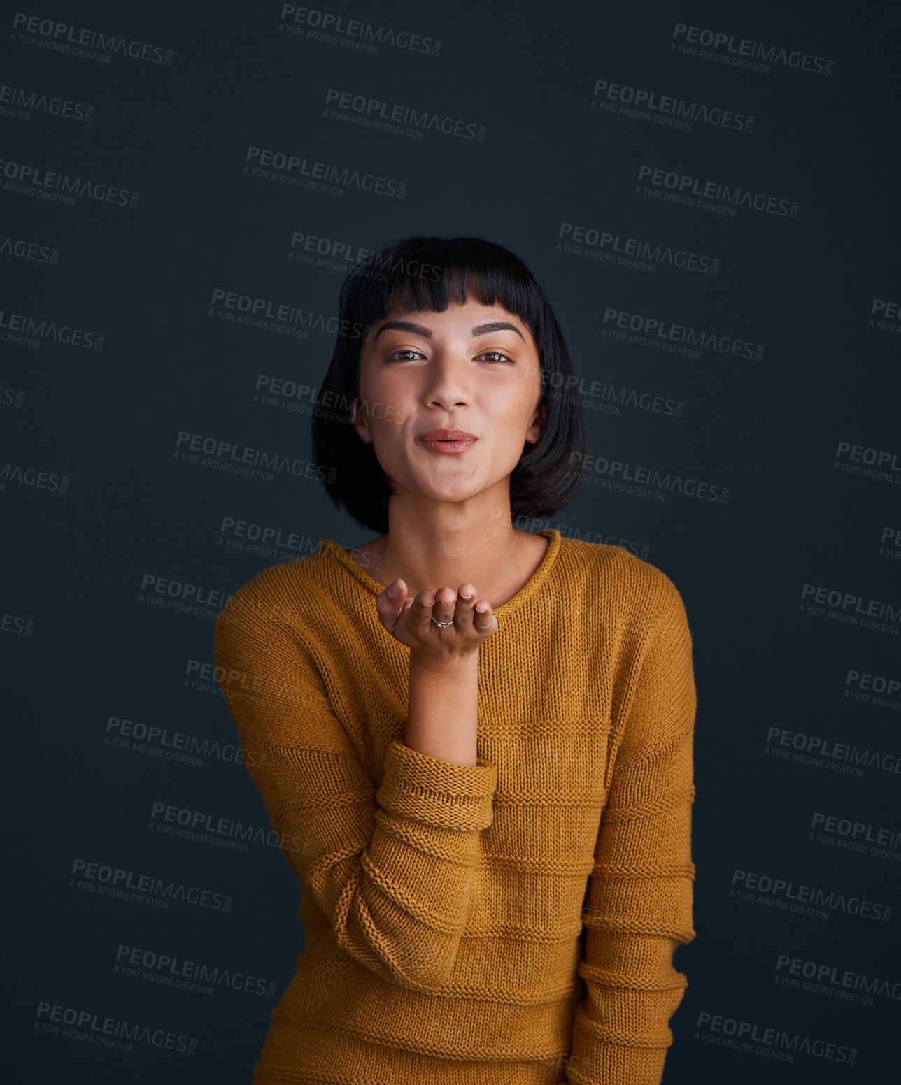 Buy stock photo Studio portrait of an attractive young woman blowing kisses against a dark background
