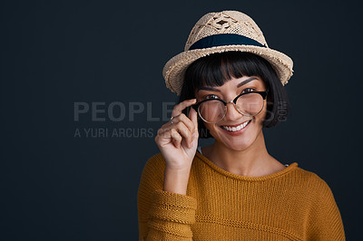 Buy stock photo Studio shot of an attractive young woman wearing glasses and a hat against a dark background