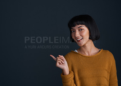 Buy stock photo Studio shot of an attractive young woman pointing against a dark background