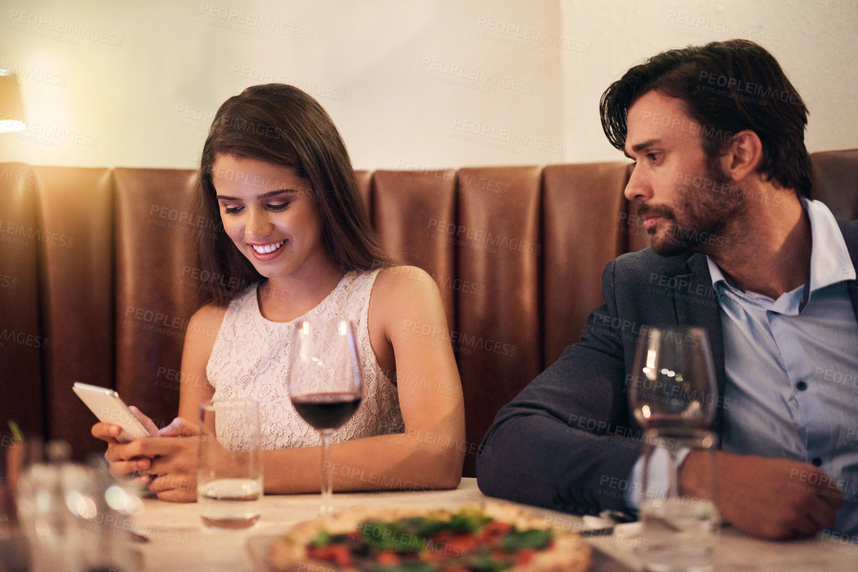 Buy stock photo Cellphone, chatting and couple on a date at a restaurant for valentines day, romance or anniversary. Communication, upset and annoyed man watching his happy girlfriend sitting on her phone at dinner.
