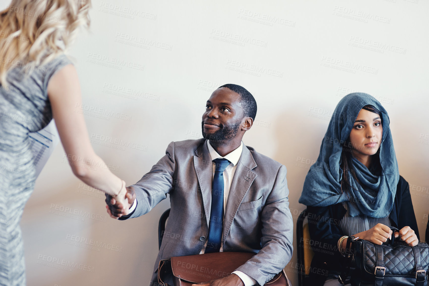 Buy stock photo Shot of a cheerful young business receiving a handshake from a businesswoman while waiting for a interview inside of a office during the day