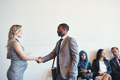Buy stock photo Shot of a cheerful young business receiving a handshake from a businesswoman while waiting for a interview inside of a office during the day