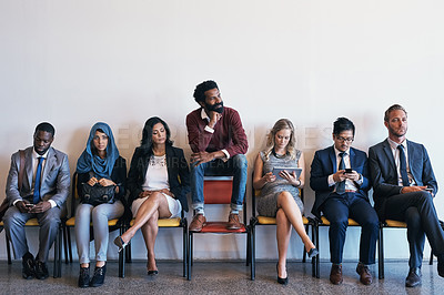 Buy stock photo Shot of a group of confident businesspeople waiting in line for their interviews while a man sits on top of a chair inside of a office during the day