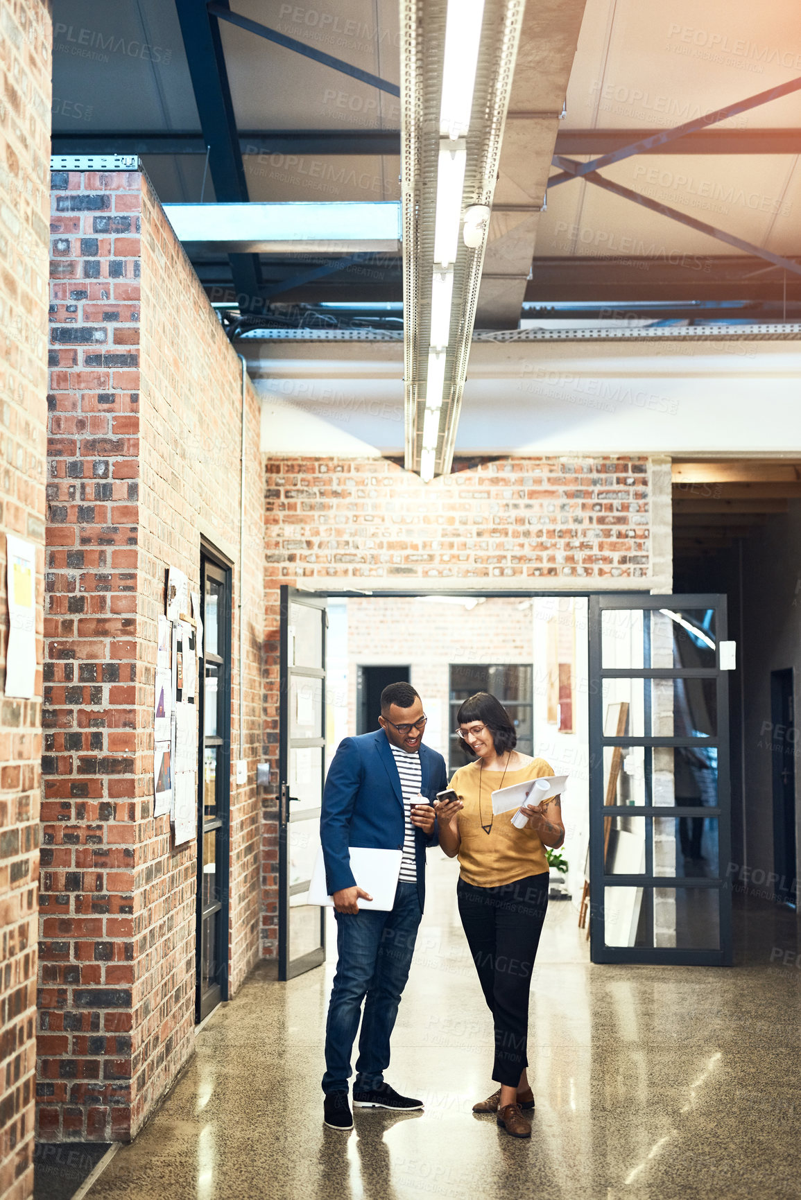 Buy stock photo Shot of two designers looking at something on a cellphone in an office