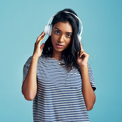 Buy stock photo Portrait, headphones and Indian woman streaming music, audio and listening to sound on blue studio background. Serious face, person and girl with headset and gen z with attitude and app for radio
