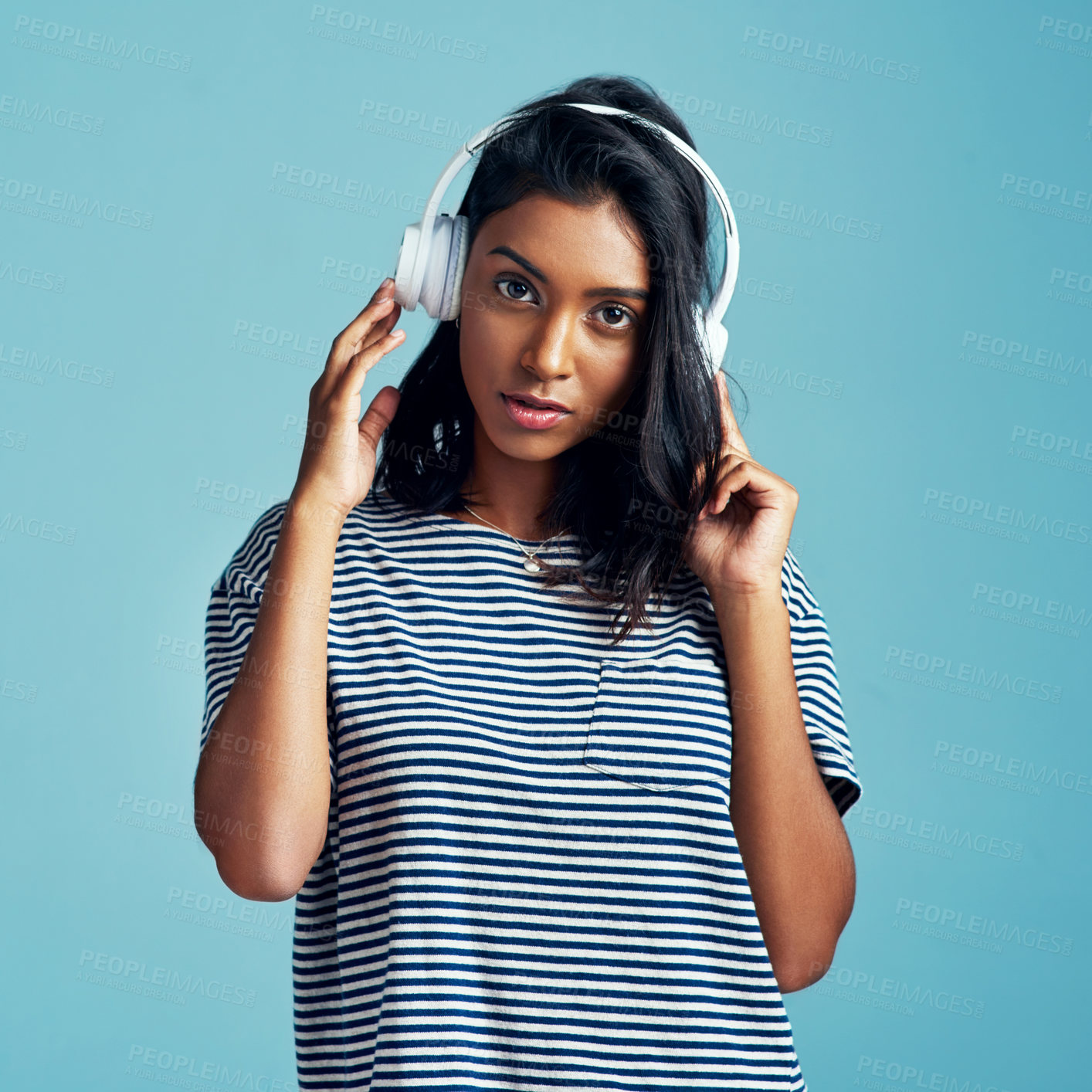 Buy stock photo Portrait, headphones and Indian woman streaming music, audio and listening to sound on blue studio background. Serious face, person and girl with headset and gen z with attitude and app for radio