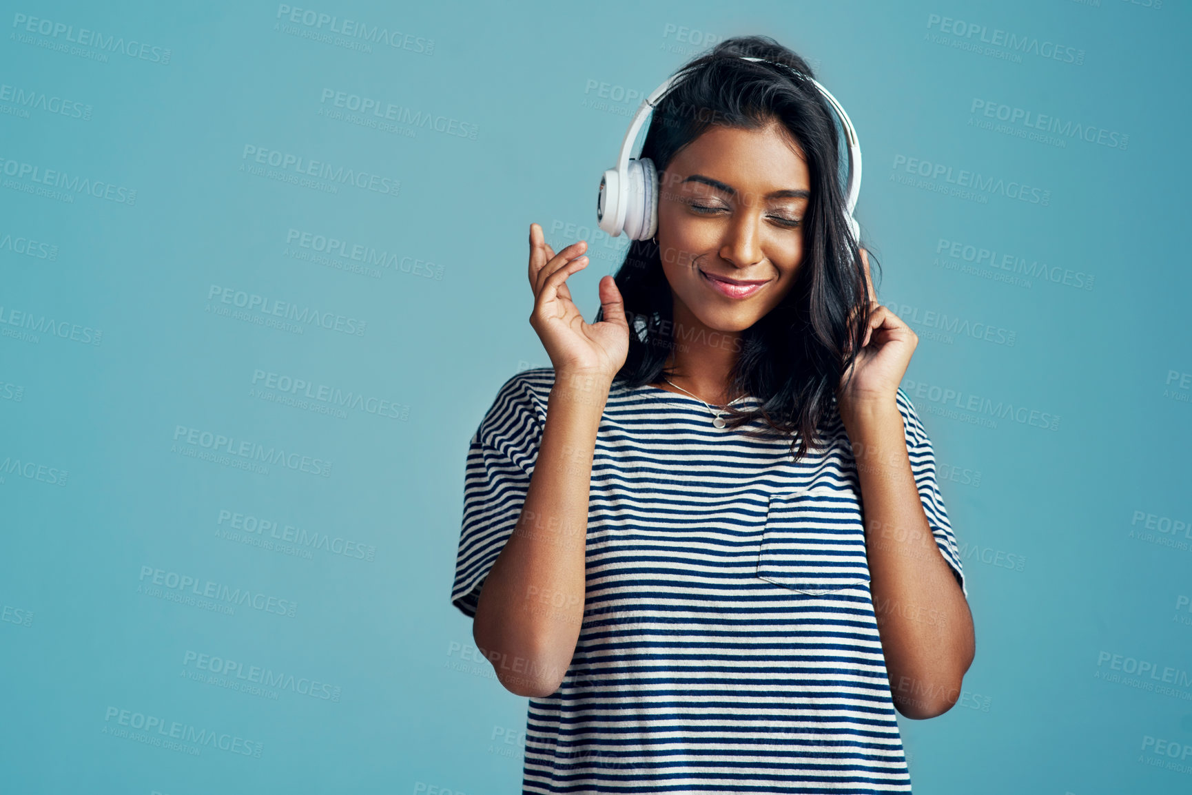 Buy stock photo Cropped shot of a beautiful young woman wearing headphones against a blue background