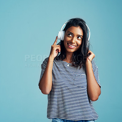Buy stock photo Woman, thinking and headphones with music in studio with happiness and web audio. Blue background, Indian female person and young model listening, hearing and streaming a song with smile and mockup