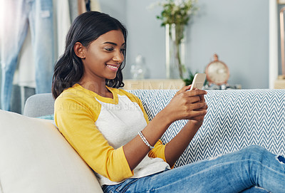 Buy stock photo Cropped shot of a young woman using a cellphone while chilling on the sofa at home