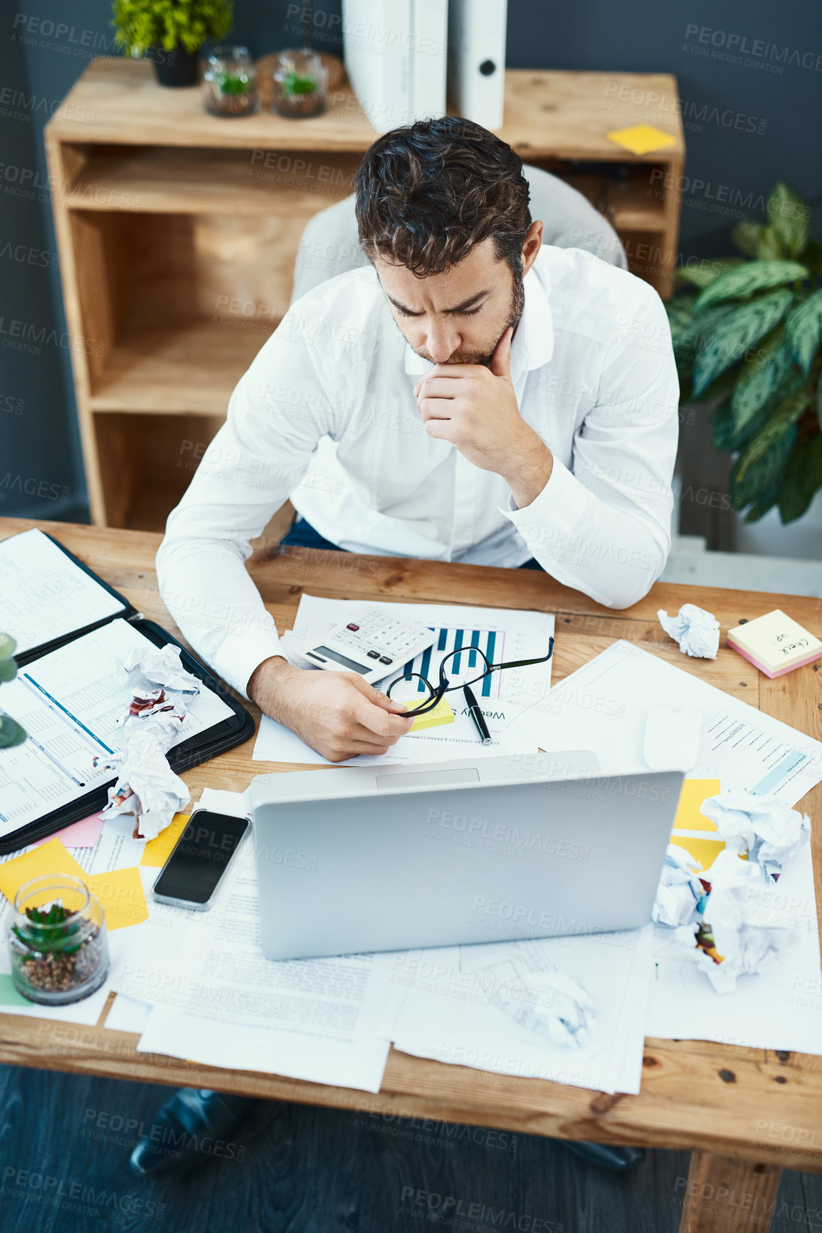 Buy stock photo Shot of a young businessman looking serious while working on a laptop in an office