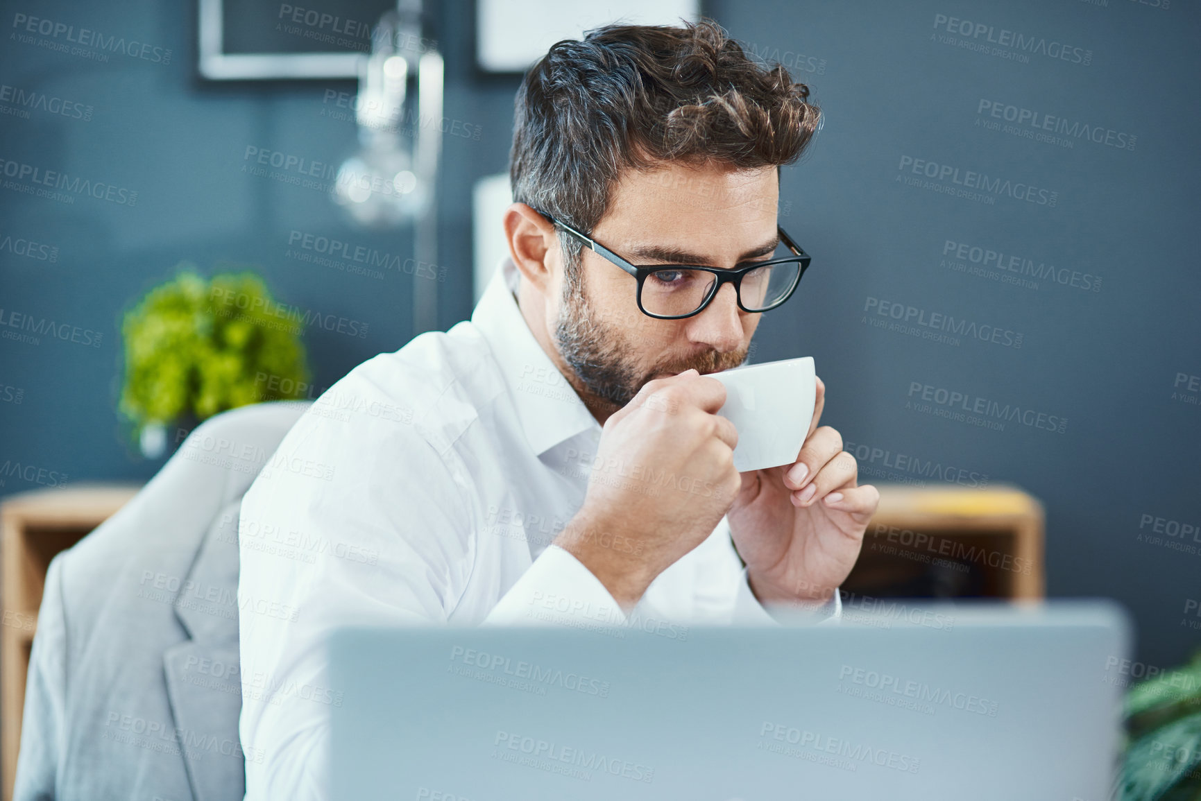 Buy stock photo Shot of a young businessman drinking a cup of tea while working in an office