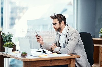 Buy stock photo Shot of a young businessman texting on his cellphone while working in an office