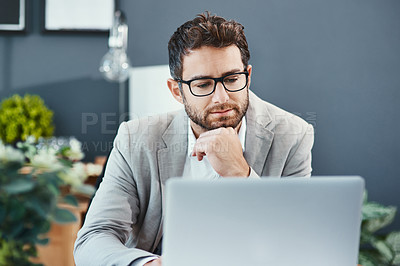 Buy stock photo Shot of a young businessman working on a laptop in an office