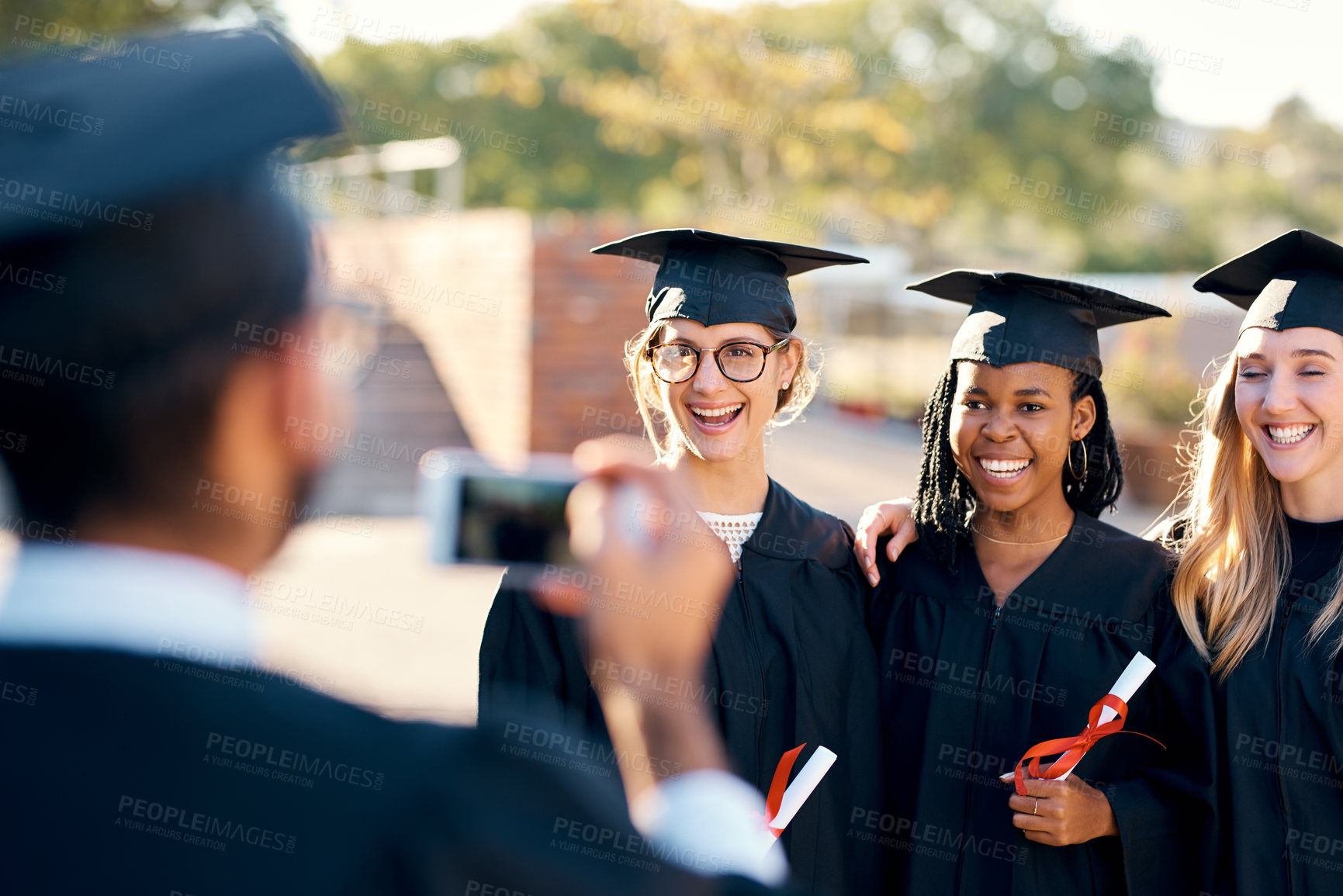 Buy stock photo People, picture and graduation outside with students, friends and smartphone for memory photo with graduate pride. Happy, smile and together with diploma achievement, university and capture in gown
