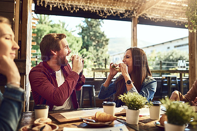 Buy stock photo Cropped shot of an affectionate young couple biting into their sandwiches while out for lunch at a cafe with friends
