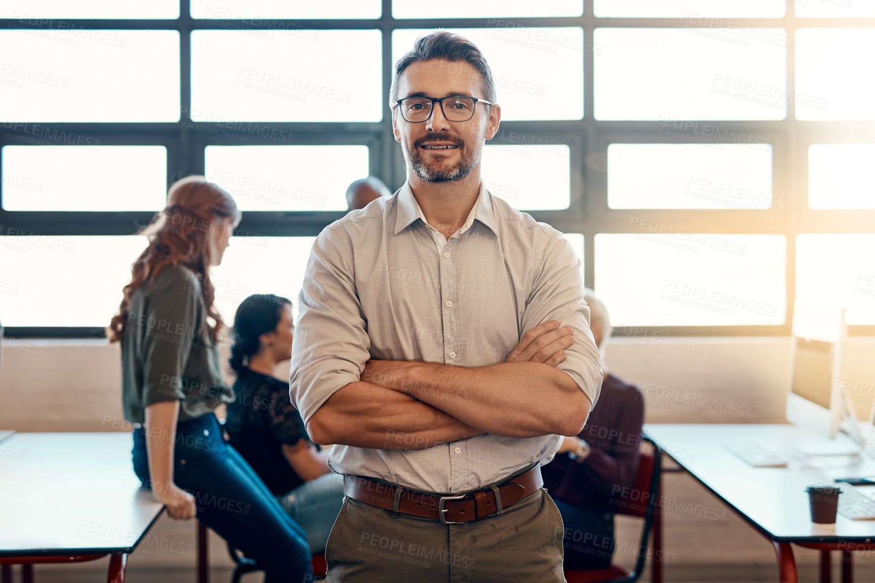 Buy stock photo Portrait of a confident mature businessman standing in a modern office with his colleagues in the background