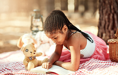 Buy stock photo African kid, teddy bear and reading book at park for learning, study and relax in forest for education. Picnic blanket, outdoor and girl child with story, magic fairytale and fantasy for knowledge