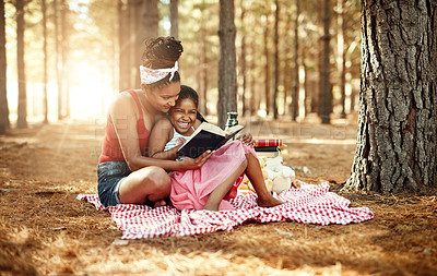 Buy stock photo Shot of a mother and her little daughter reading a book together in the woods
