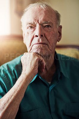 Buy stock photo Cropped portrait of a senior man sitting with his hand on his chin in a living room