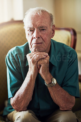 Buy stock photo Cropped portrait of a senior man sitting with his hands on his chin in a living room