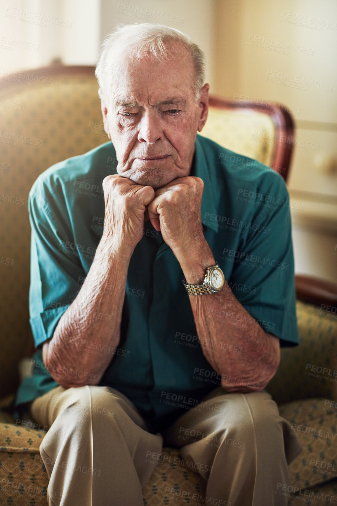 Buy stock photo Cropped shot of a senior man looking sad while sitting with his hands on his chin in a living room