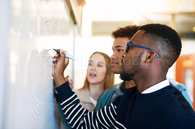 Buy stock photo Shot of a young man writing on a whiteboard while students look on