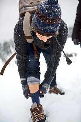 Buy stock photo Shot of a young man pulling up his socks while out on the snow