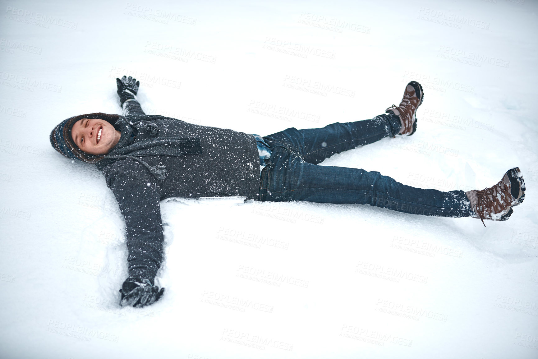 Buy stock photo Shot of a young man lying in the snow making a snow angel