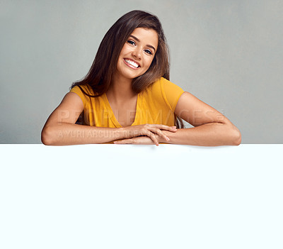 Buy stock photo Studio portrait of an attractive young woman leaning on a blank placard against a grey background