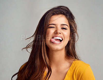 Buy stock photo Studio portrait of an attractive young woman sticking her tongue out against a grey background