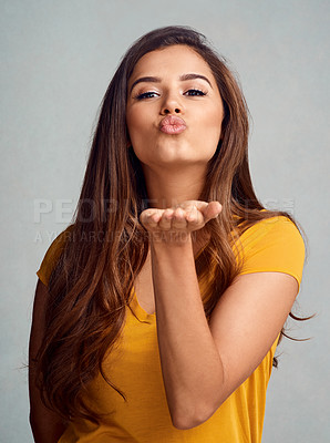 Buy stock photo Studio portrait of an attractive young woman blowing a kiss against a grey background