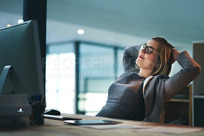 Buy stock photo Shot of a young businesswoman sitting with her hands behind her head in an office at night