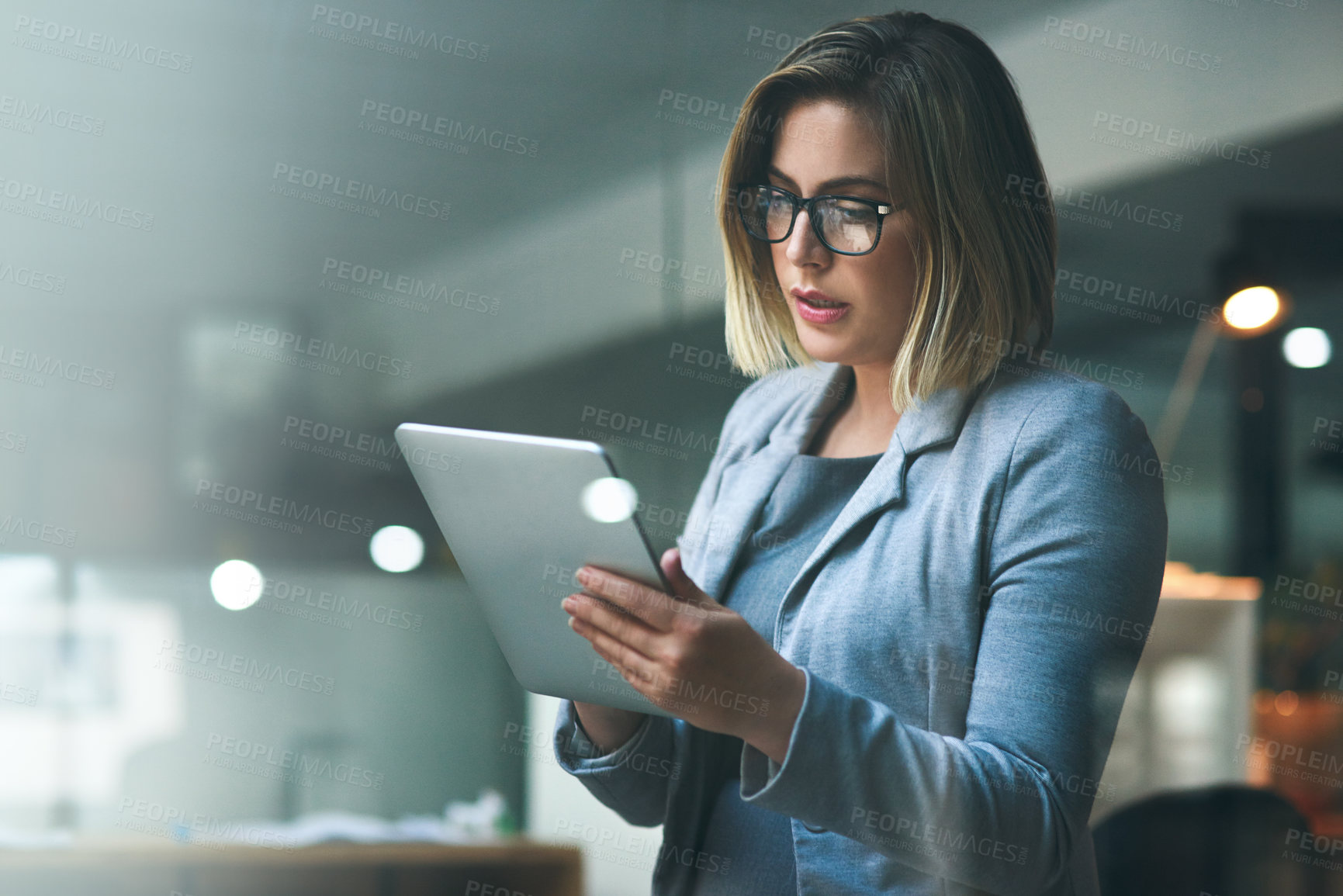 Buy stock photo Shot of a young businesswoman working late on a digital tablet in an office