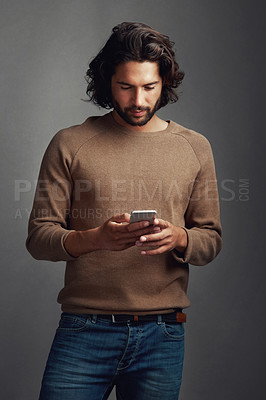 Buy stock photo Studio shot of a handsome young man using a mobile phone against a gray background